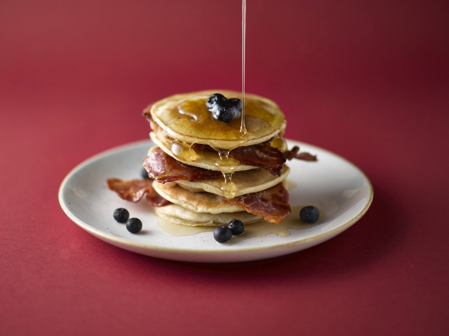 A pancake stack with bacon, maple syrup and blueberries