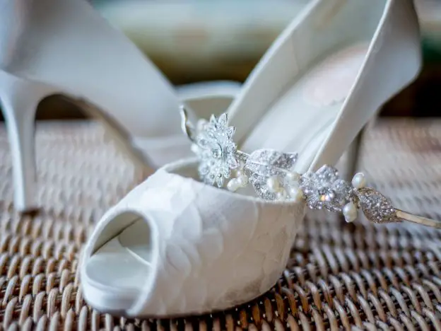 Lace patterned ivory coloured wedding shoes, with a diamonte and pearl headband laid across them