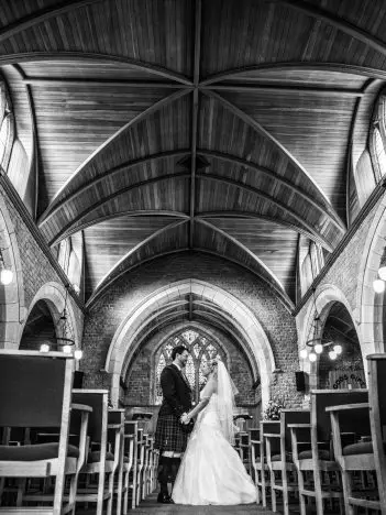 A black and white image of a bride and groom on their wedding day, standing in the middle of a church