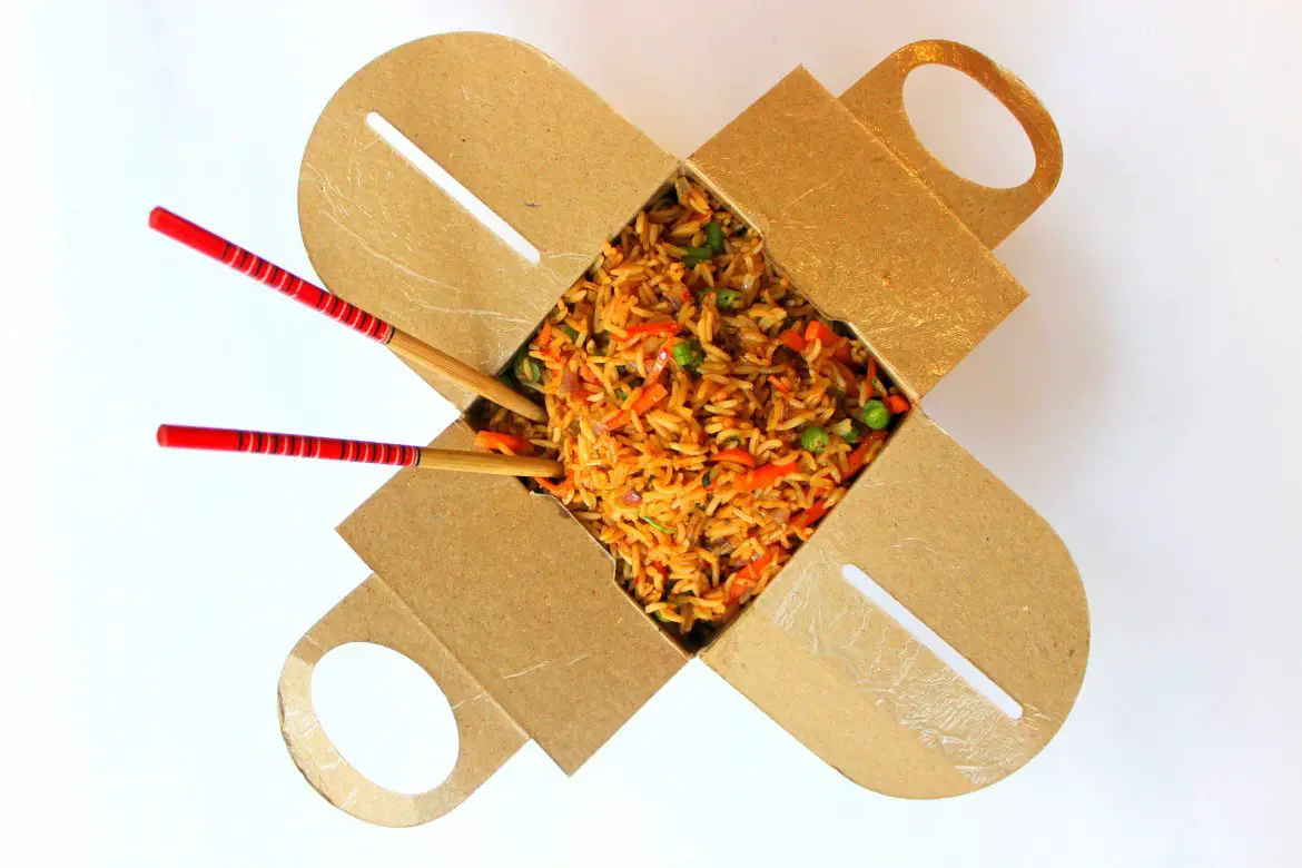 A takeaway container open with a Chinese dish inside and 2 chopsticks
