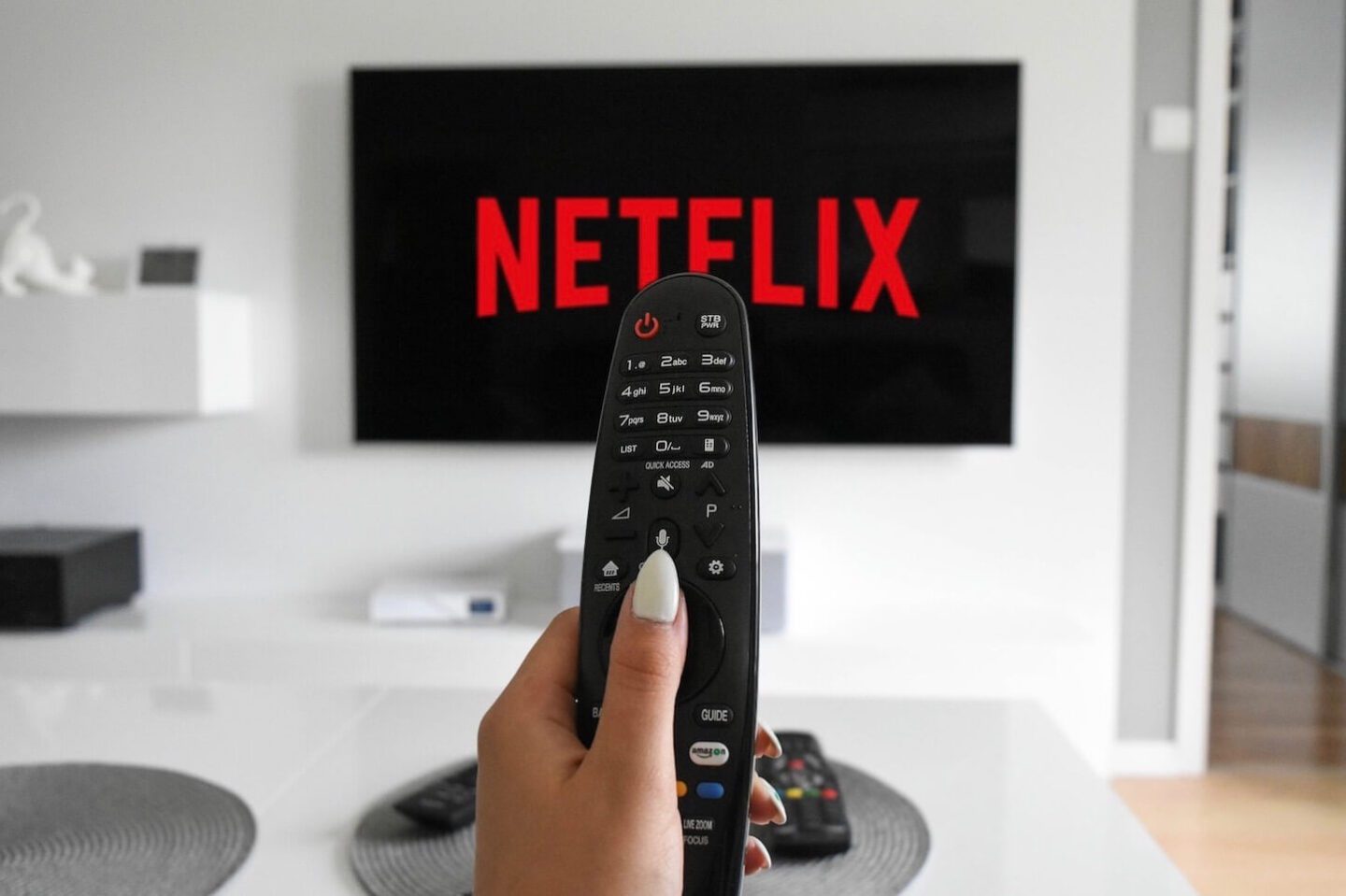 A TV screen with the Netflix logo on it, and a hand holding up the tv remote