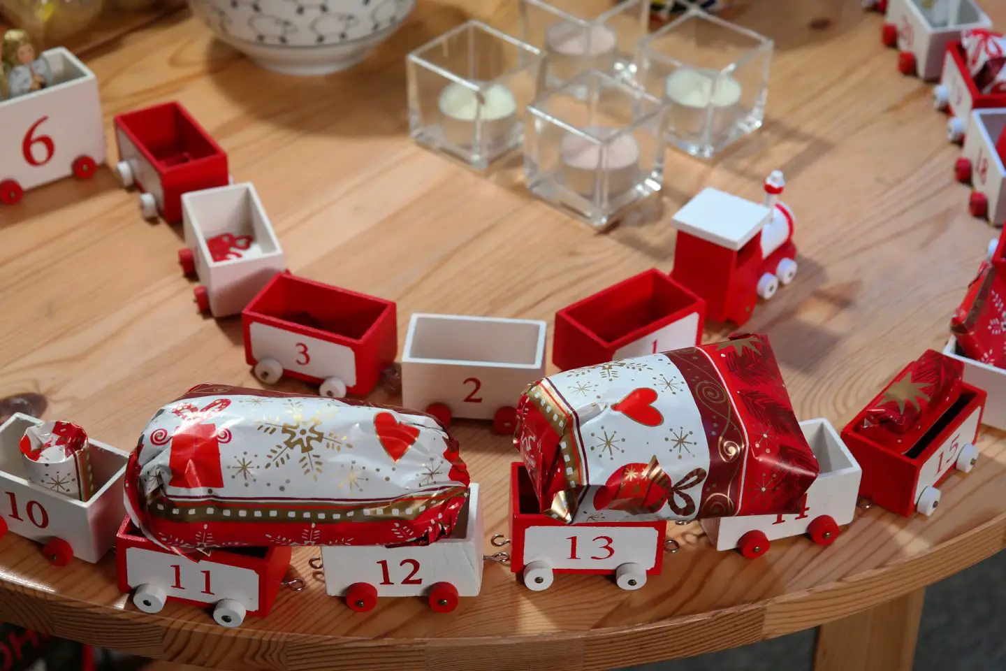 A table with a red and white wooden train advent calendar on it with gifts on the carriages.