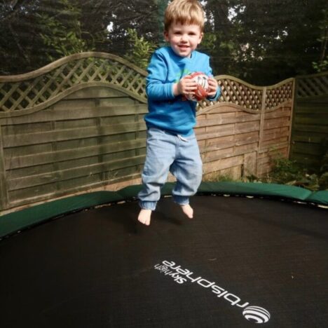 A boy holding a ball and jumping on a trampoline