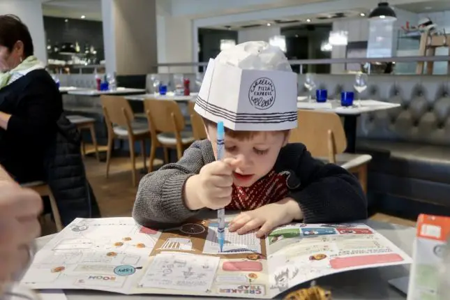 A young boy in pizza express drawing on an activity sheet