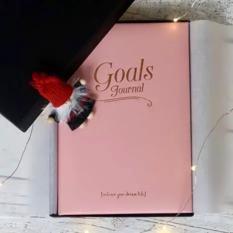 A pink notebook with "Goals Journal" written on it in gold text