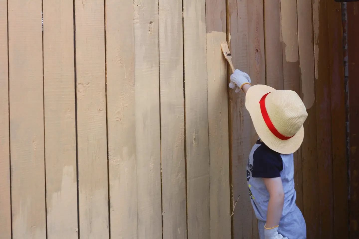 How To Prepare For Major Changes In Your Garden | A young boy wearing a hat with a red ribbon and a blue tshirt is painting a wooden fence a beige colour www.oddhogg.com