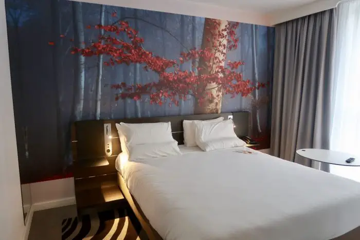 A double bed in a hotel room in Novotel York Centre, with a tree wallpaper behind it
