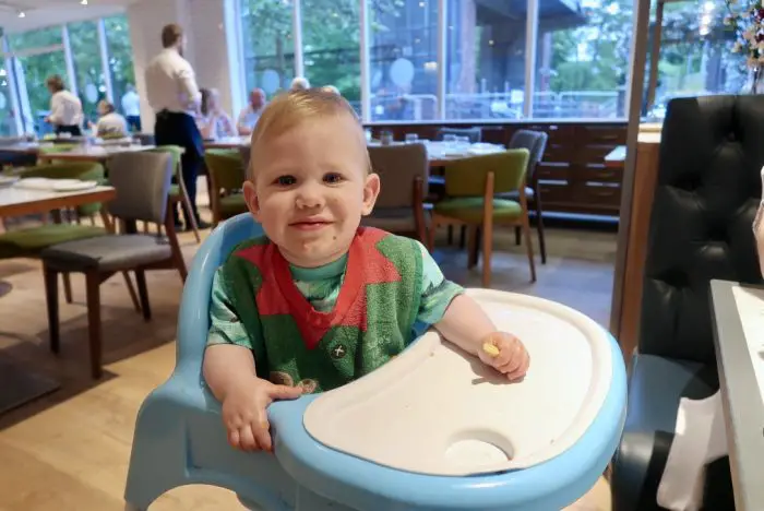 a young baby in a highchair at a restaurant. He is wearing a green and red bib