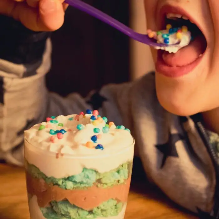 A child eating a layered dessert with sprinkles on the top