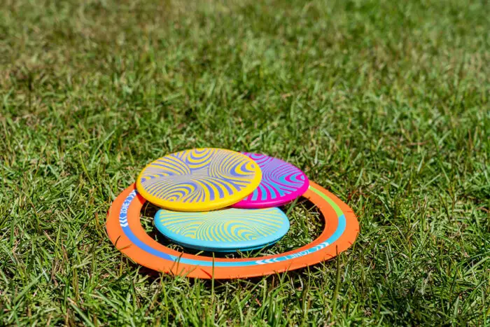 A hoop and 3 frisbees lying on grass.