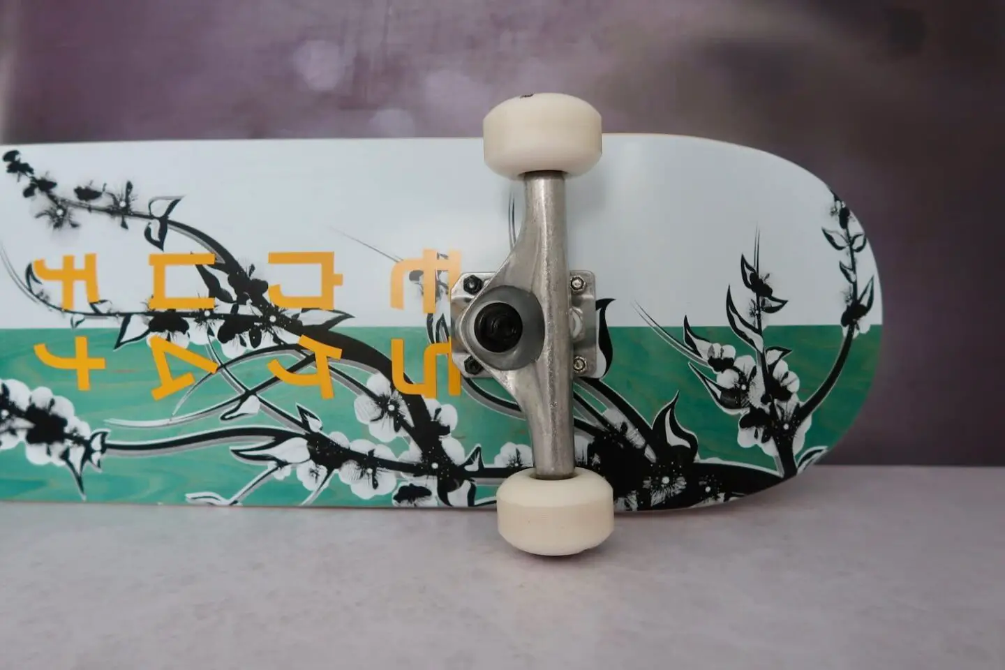 The base of a skateboard lying on it's side. It is half white and half green with a cherry blossom design