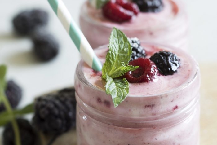 A pink smoothie in a glass jar, with a blue and white striped straw and topped with berries
