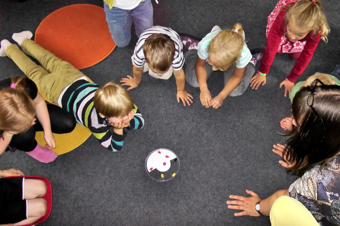 A group of children in childcare watching something on the floor with their teacher
