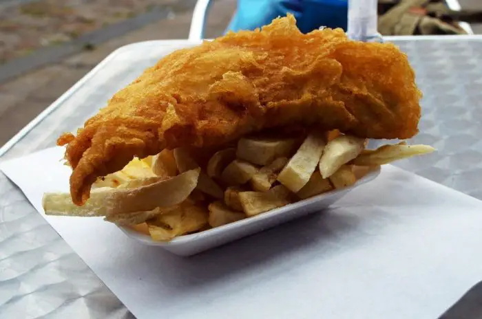a takeaway dish of fish and chips on a metal outdoor table