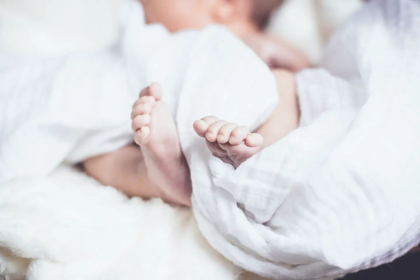 A newborn baby wrapped in a white blanket. The baby's feet are the focus of the photo