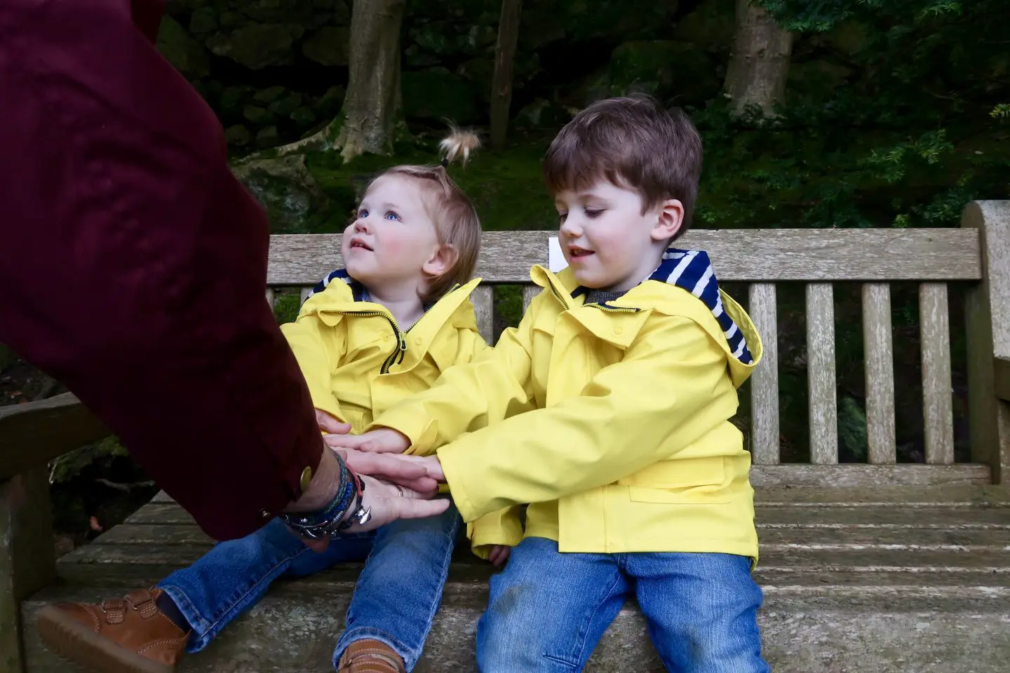 2 boys in matching yellow coats are sitting on a bench and giving their dad a high 5