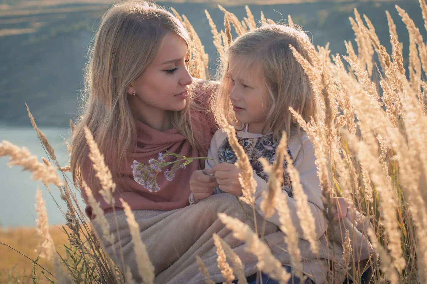 A mother and daughter sit amongst some wheat in golden light
