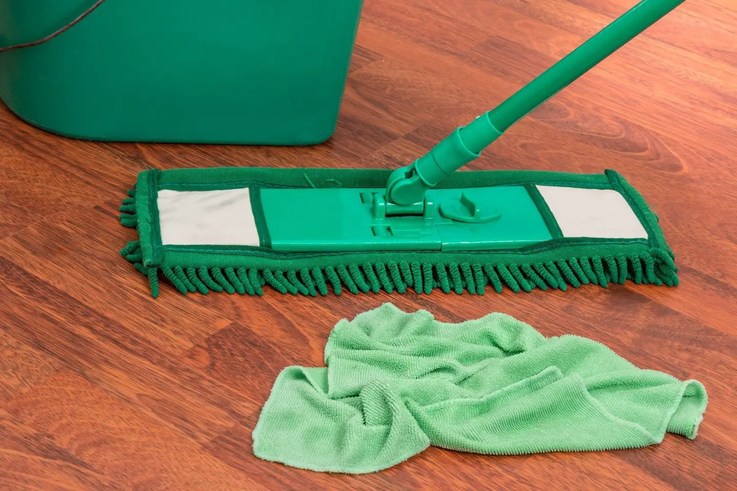 A green cloth, bucket and mop on a wooden floor