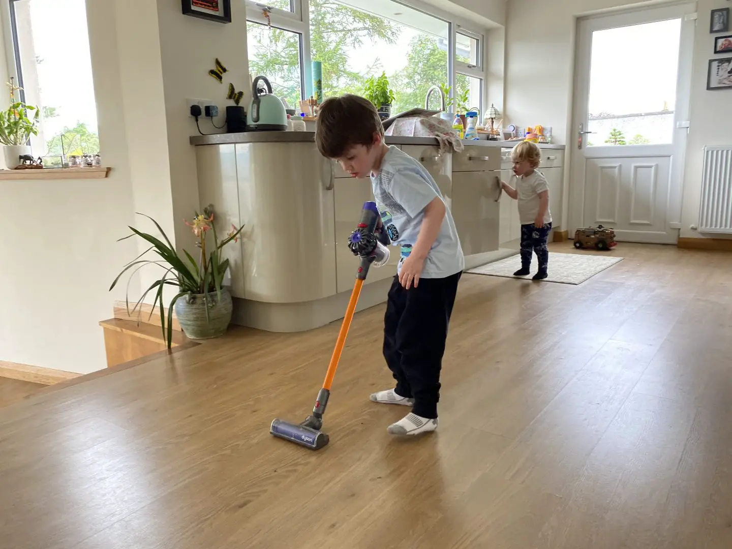 A boy in a kitchen using a toy Dyson cord-free vacuum cleaner
