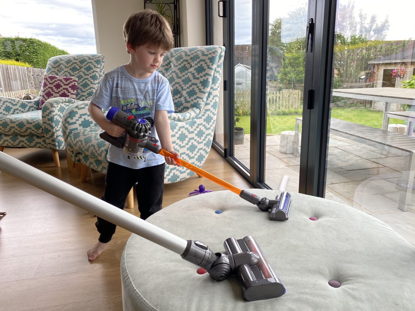 A boy using a toy Dyson cordless vacuum cleaner alongside a real one