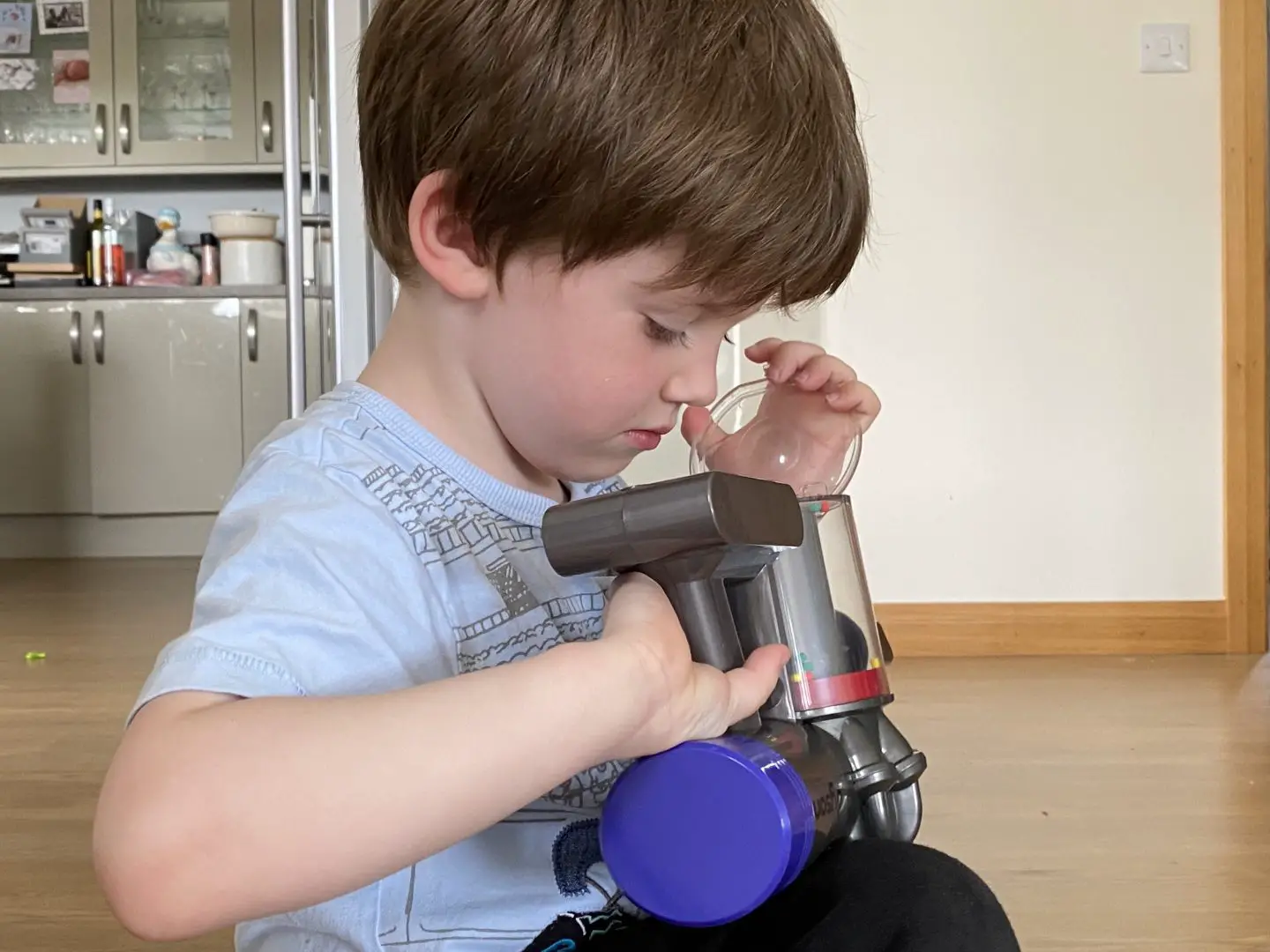 A boy looking into the dust compartment of a toy Dyson