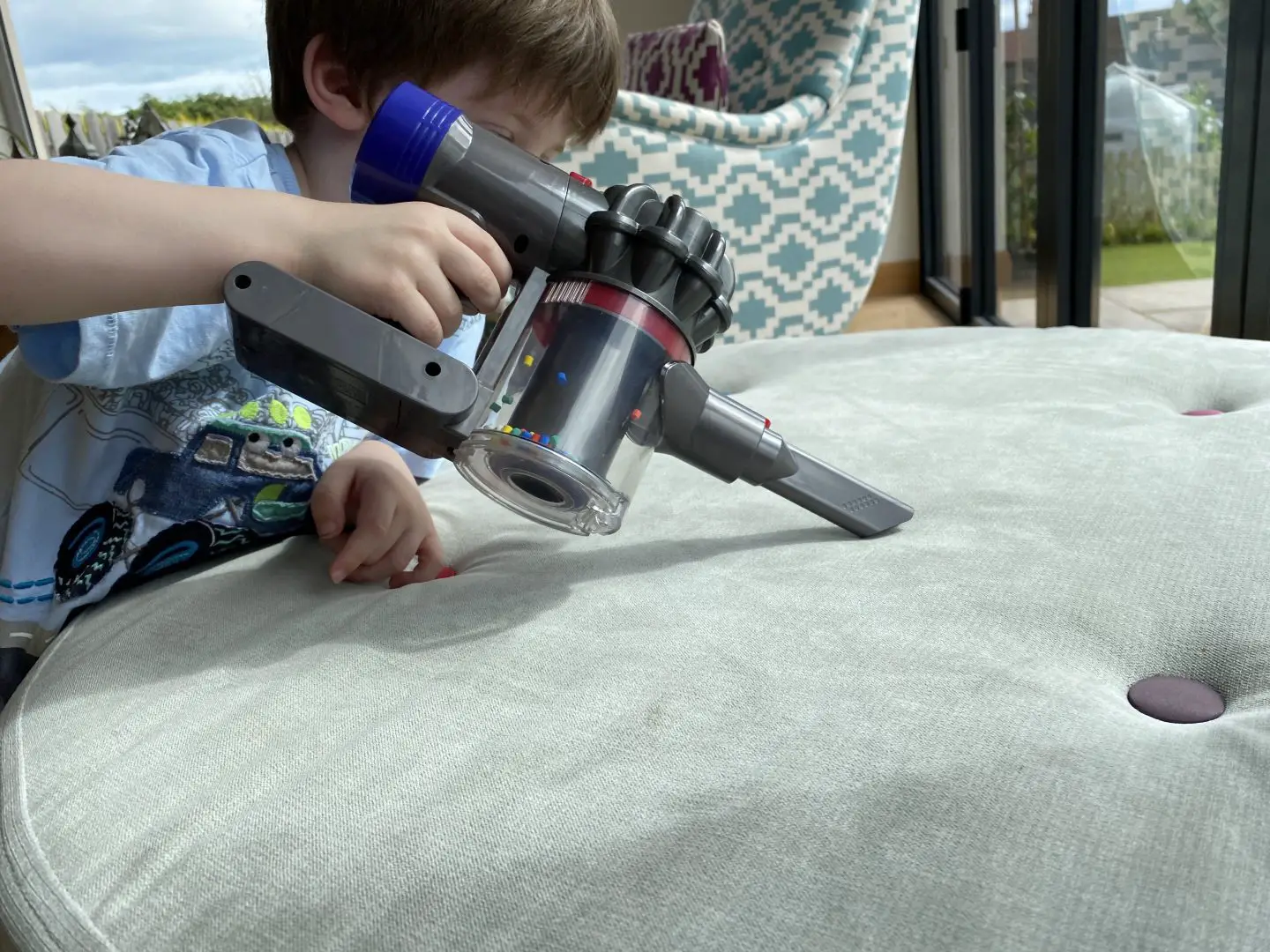 A boy hoovering a seat with a toy cordless vacuum cleaner