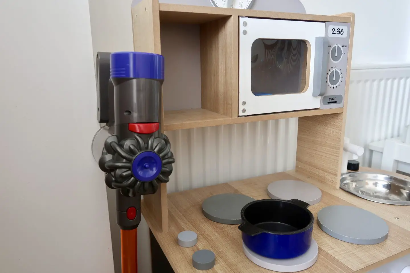 a kids toy Dyson cord-free vacuum cleaner next to a toy kitchen
