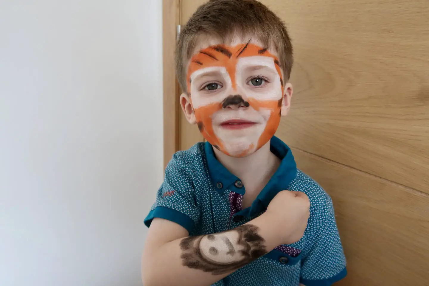 A little boy with his face painted as a tiger and a ghost painted on his arm.