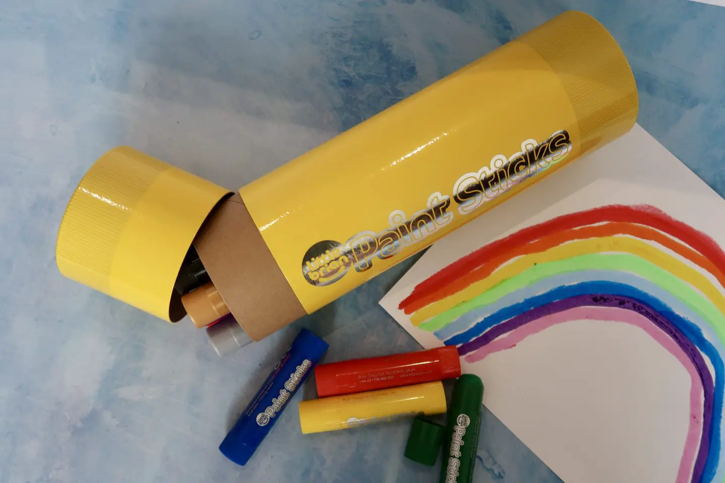 A set of Little Brian paint sticks in a giant paint stick box, next to a rainbow painted on a piece of paper