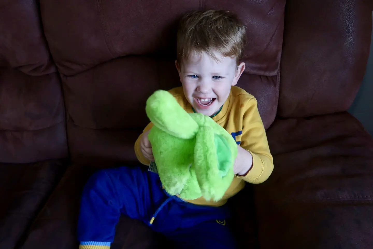 A toddler laughing at a green fluffy toy in his hands