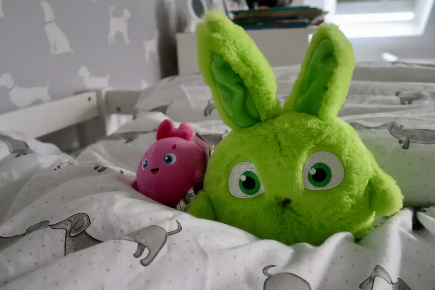 A large green Sunny Bunnies and a small pink Sunny Bunnies sitting on a child's bed