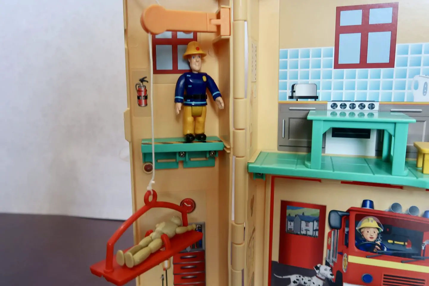 Fireman Sam figure standing on a ledge next to a pulled with a red stretcher and training dummy on it