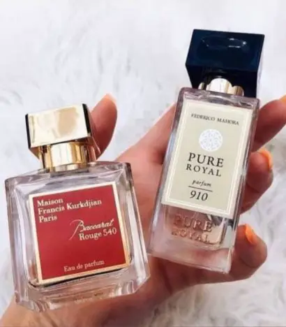 A hand holding a bottle of Baccarat Rouge perfume and FM 910