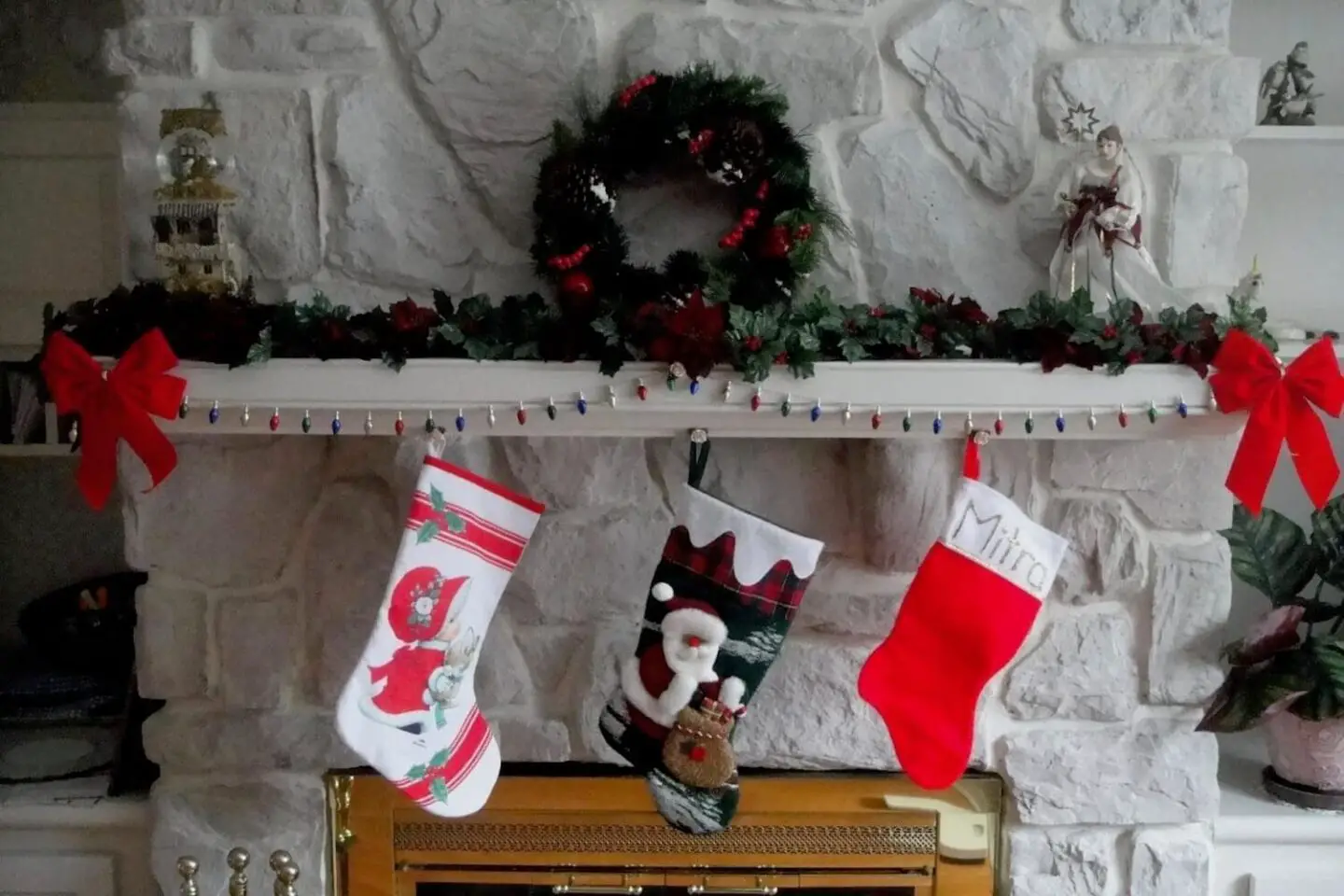 3 stockings hanging on a mantle piece, with a Christmas wreath above