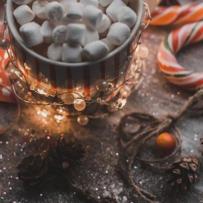 A table scattered with wooden stars, fairy lights, candy canes and a mug of hot chocolate with marshmallows