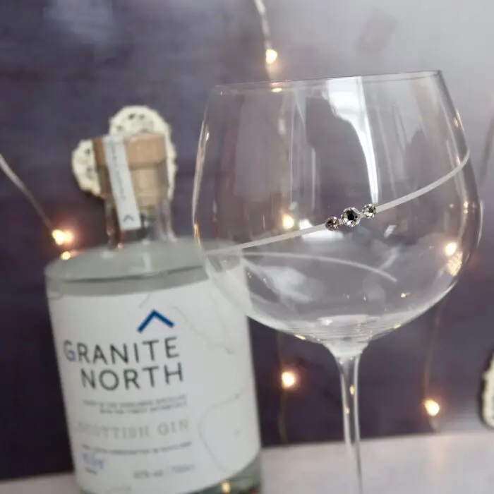 A large gin glass with a crystal on it, and a bottle of Scottish gin in the background