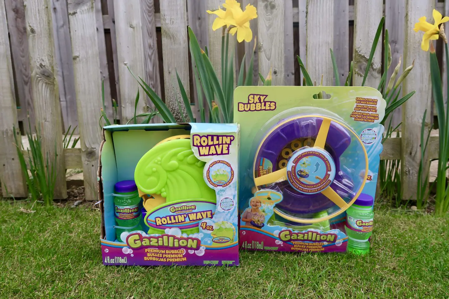 A Gazillion Bubble Rollin' Wave machine and a Sky Bubbles machine in their packaging ont he grass next to a daffodil