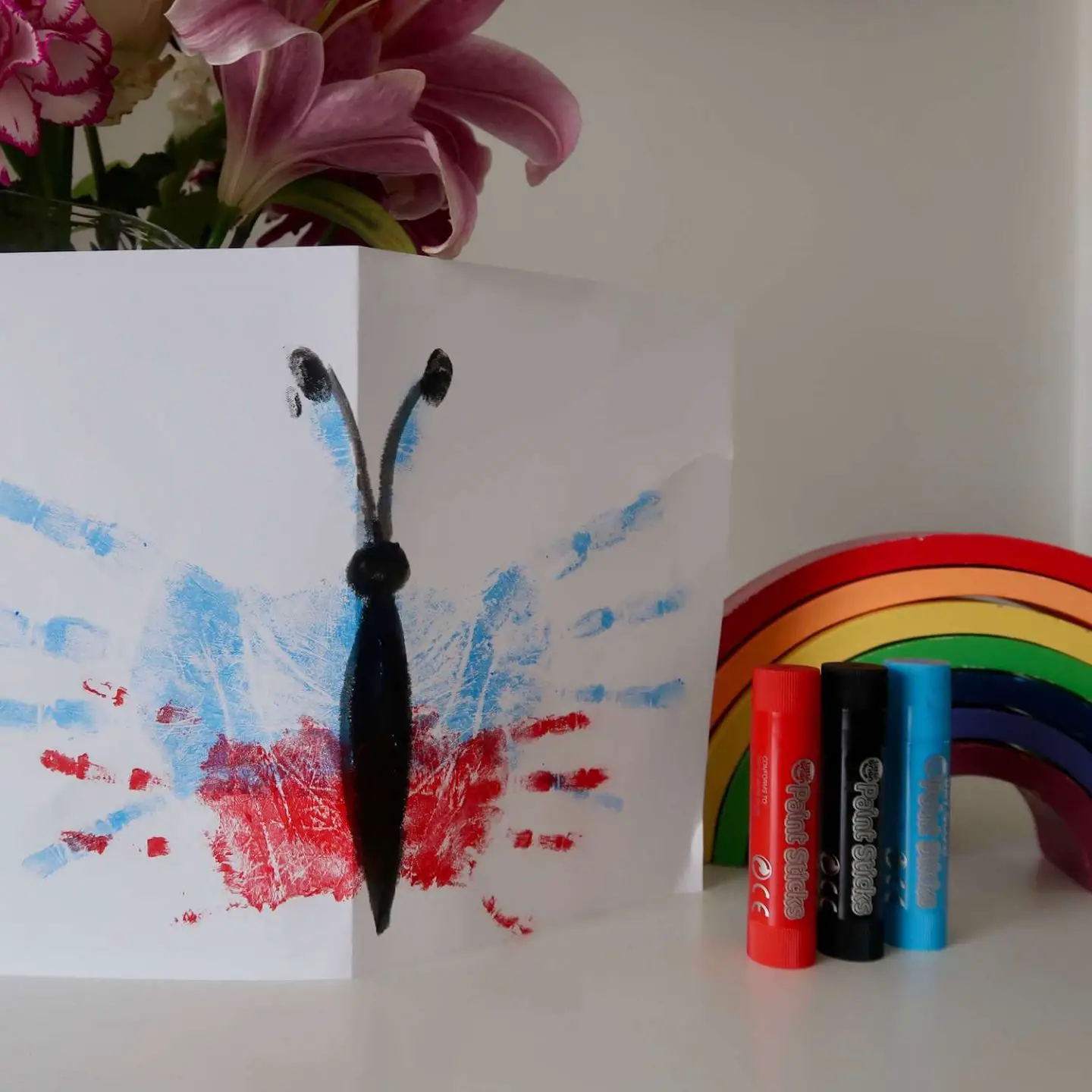 A handprint butterfly card next to some paint sticks and a wooden rainbow