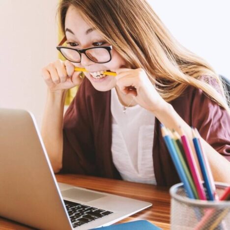 A woman looking at a laptop and biting down on a pencil