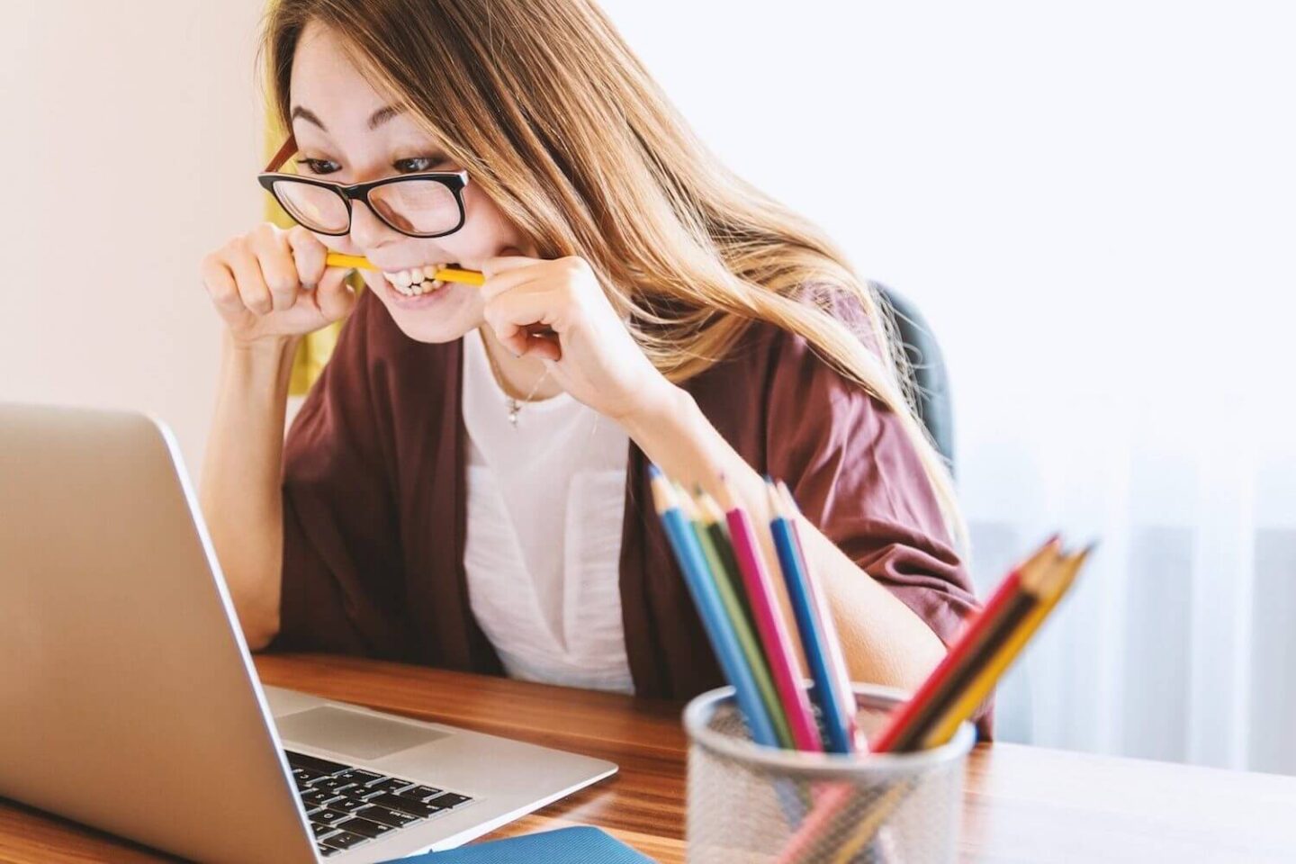 A woman looking at a laptop and biting down on a pencil