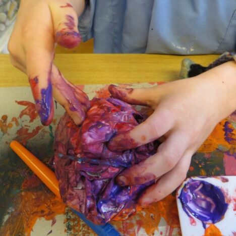 Hands holding a painted model, with paint splatters and brushes on the table below