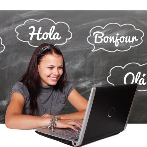 A girl looking at a laptop with hello written in different languages on a blackboard behind