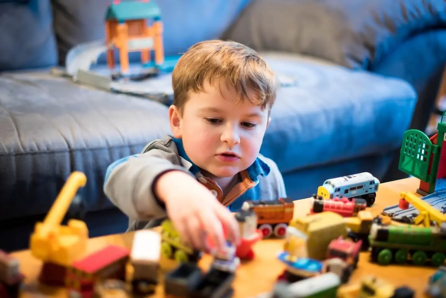A boy sitting at a low table and playing with toy trains