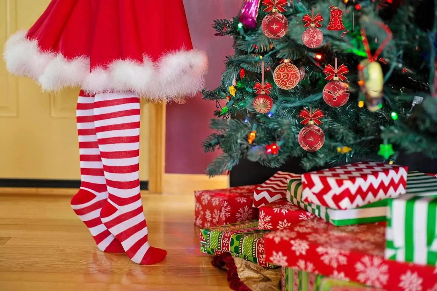 Mrs Claus legs on tiptoe next to a Christmas tree with presents underneath.