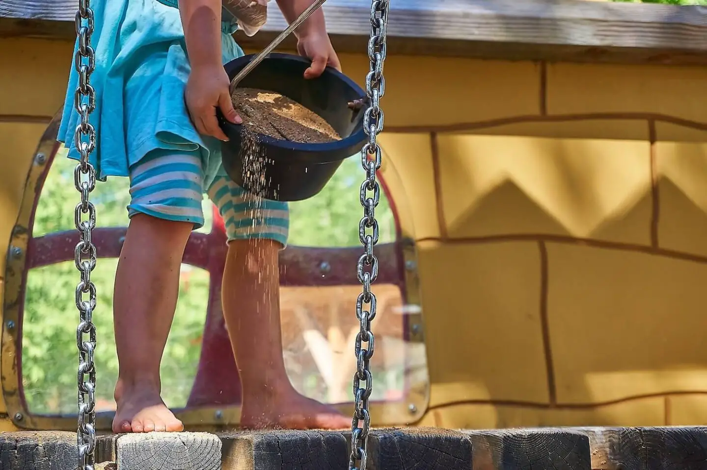 The legs of a child on a wooden climbing frame, holding a bucket of sand