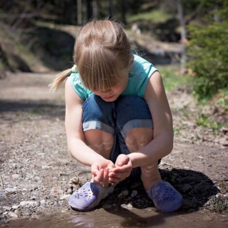 A girl crouching down to a puddle to explore