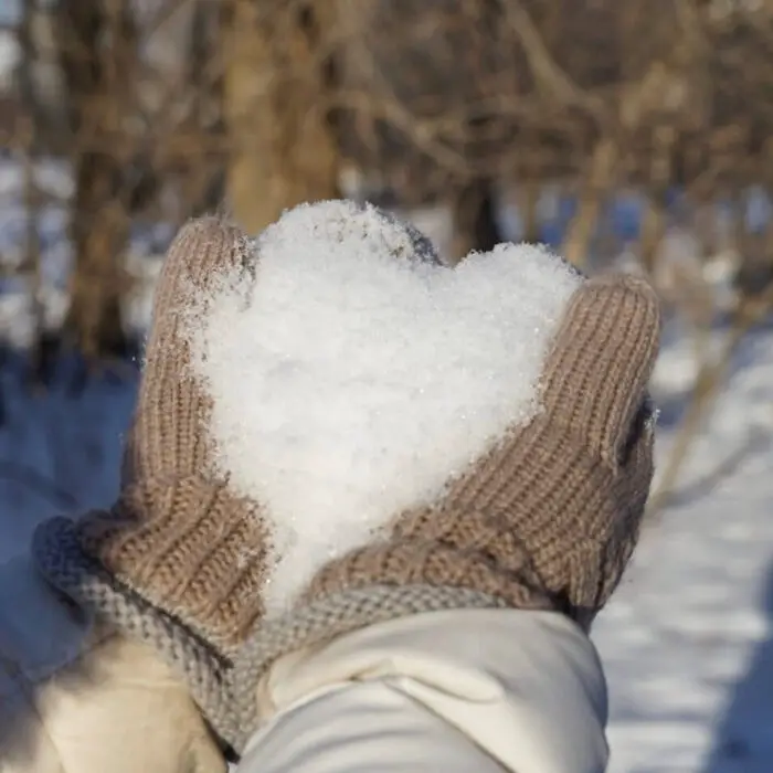 gloves hands holding snow in the shape of a heart