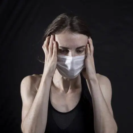 A woman wearing a face mask with her hands on either side of her head