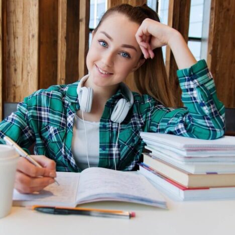 A teenager working at a table surrounded by books