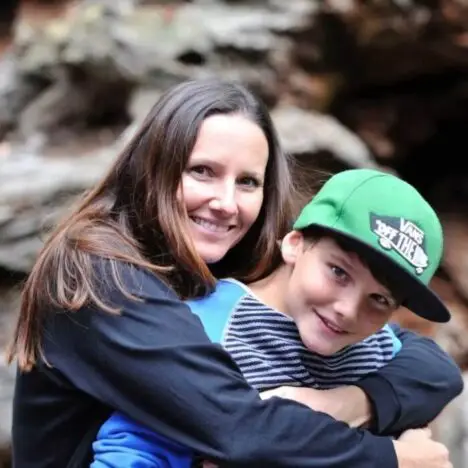 A mother with her arms around her son. He is wear a green cap, and they are both smiling for the camera